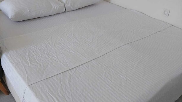A bed with white bedding, a wooden headboard, and a white wall.