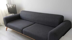 A modern living room with a grey sofa, a flat-screen TV, and a light-colored floor.