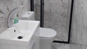 A bathroom with a shower enclosure, a sink, and a toilet.