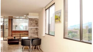 Un salon moderne comprenant un canapé, une table à manger avec des chaises, une cheminée et de grandes fenêtres donnant sur un paysage.