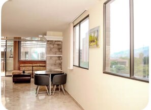 A modern living room with a sofa, a dining table with chairs, a fireplace, and large windows offering a view. - 108 LOVELY 2 BEDROOM APARTMENT NEAR PARK POBLADO (Medellín)