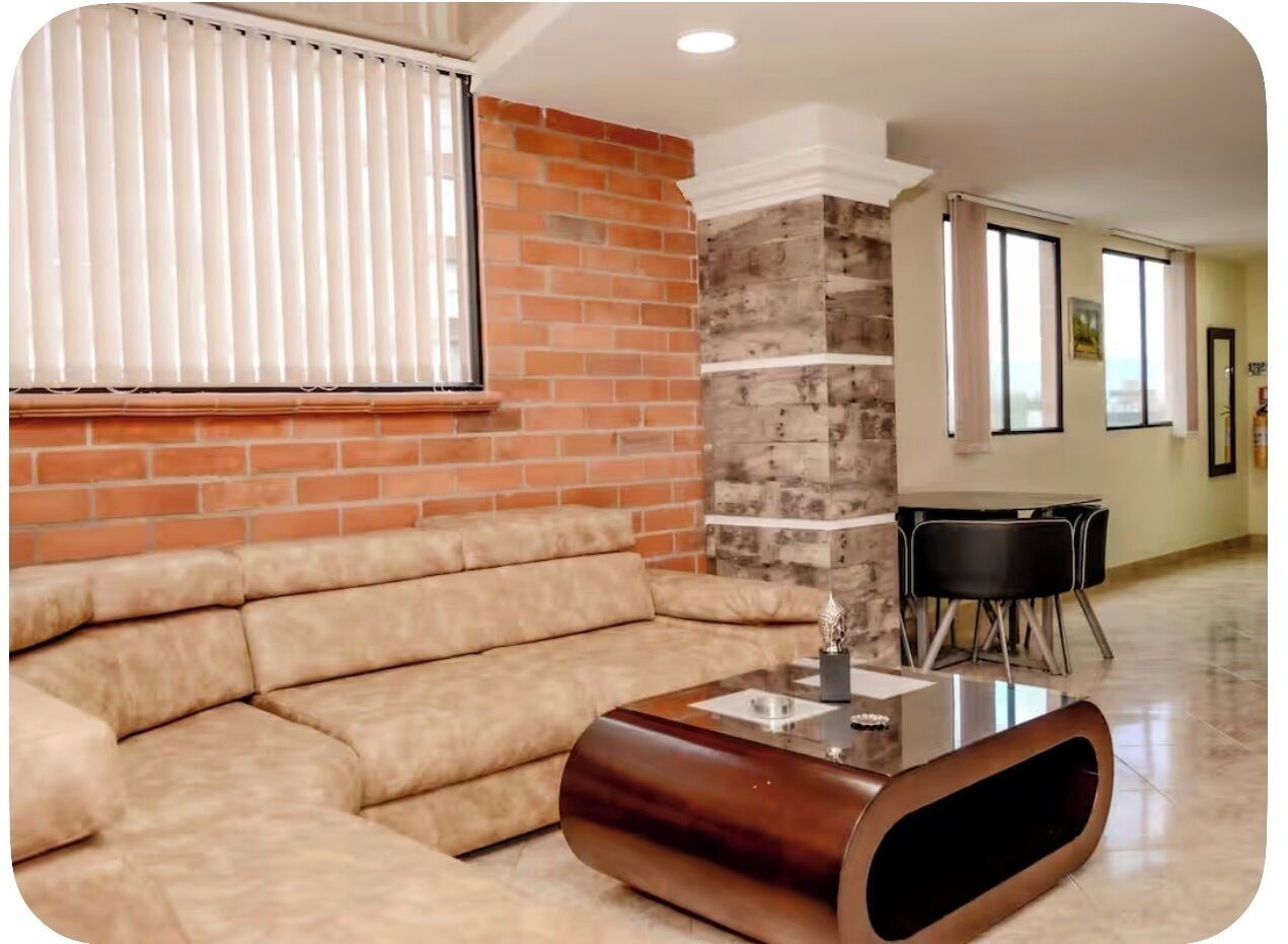 A living room with a sectional sofa, a glass-top coffee table, a brick accent wall, and a dining area with a table and chairs.