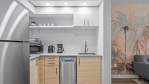 Een kleine keuken met een vaatwasser, magnetron, koffiezetapparaat en een wastafel met een moderne kraan.