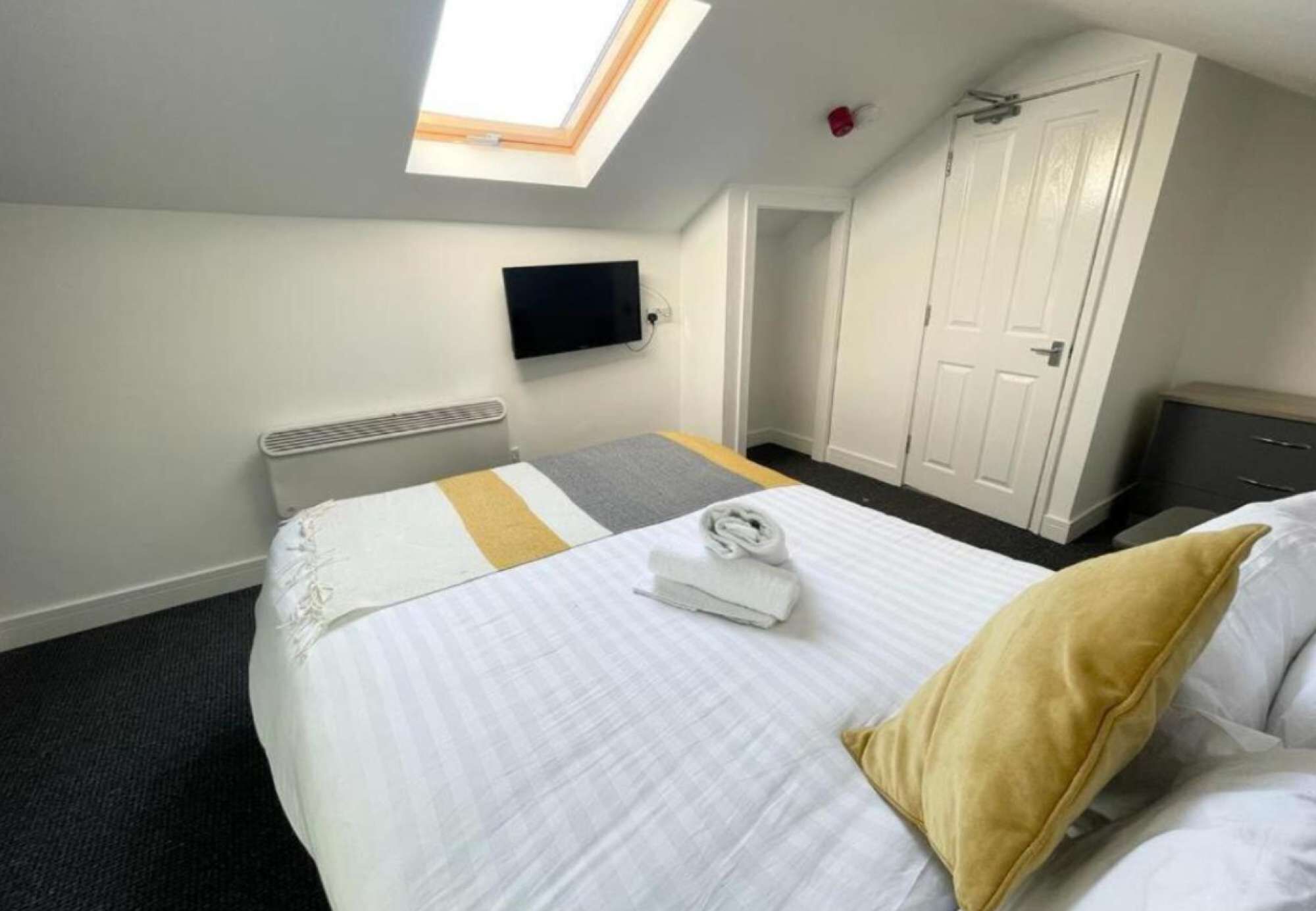 A hotel room with a bed, a flat-screen TV mounted on the wall, a radiator, a door, and a window.