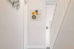Un couloir avec une porte au fond, un élément décoratif fixé au mur et un escalier sur la droite.