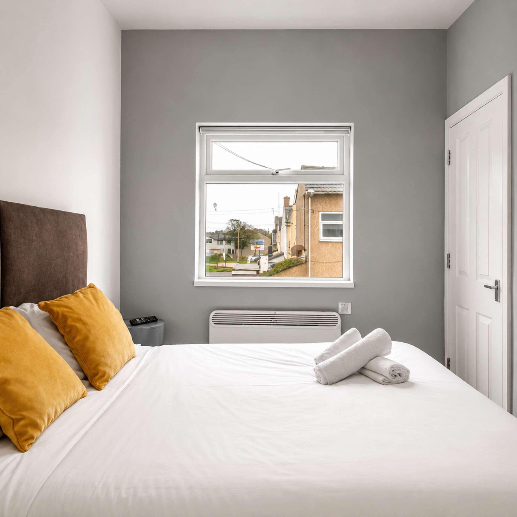 A bedroom with a bed, a window, a radiator, and a door.