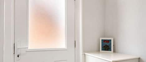 A white door with a frosted glass panel, a small cabinet with a framed picture, and a wall-mounted air conditioning unit.
