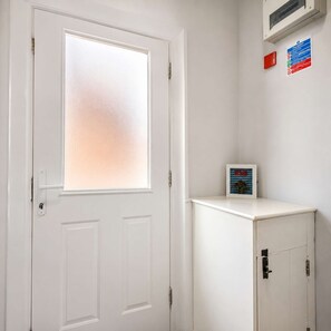 Une porte blanche avec un panneau en verre dépoli, un petit meuble avec un tableau encadré et un appareil de climatisation fixé au mur.