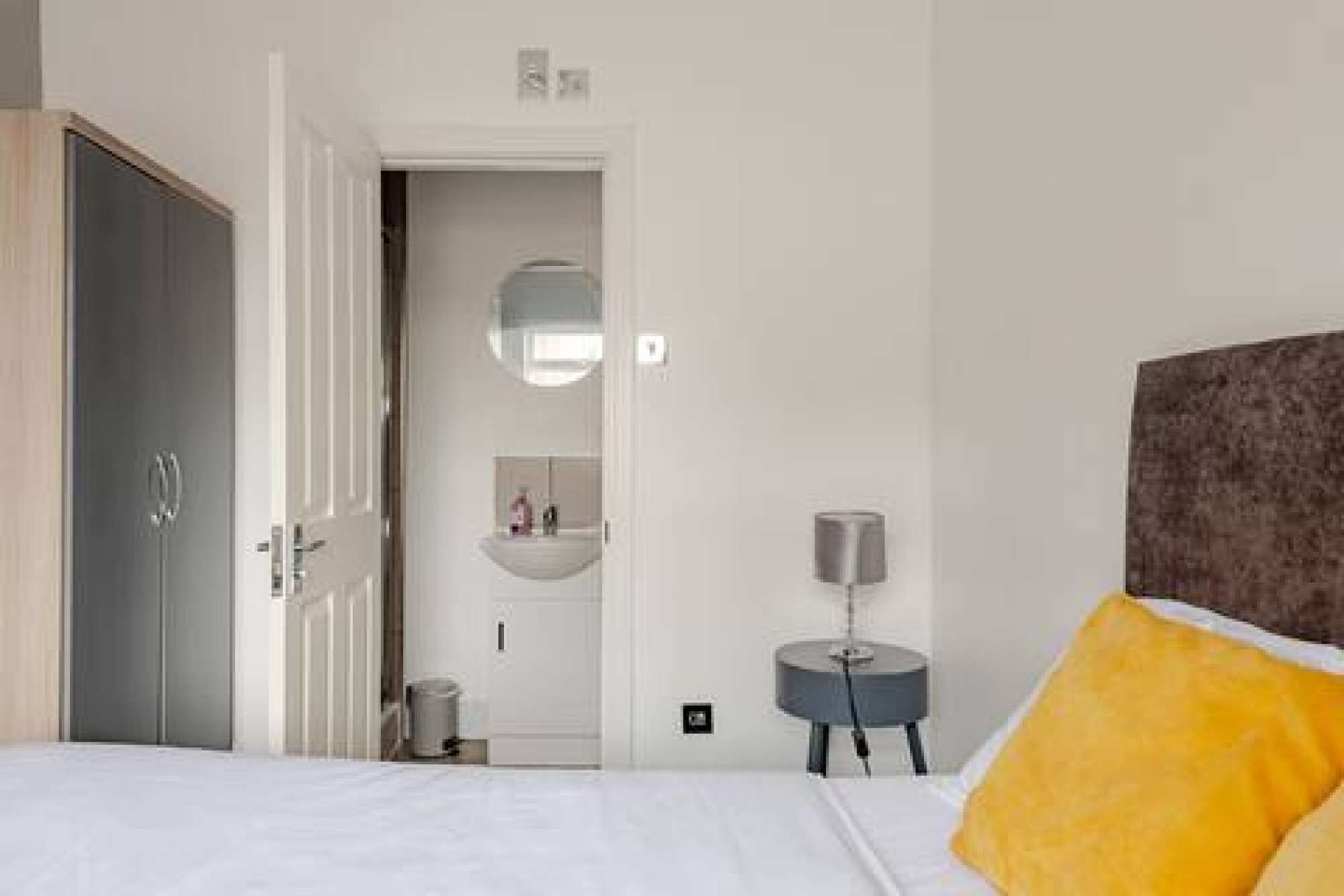A hotel room with a bed, a bedside table, a mirror, and a door leading to a bathroom.