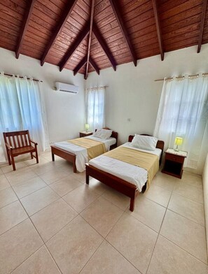 Ein Zimmer mit zwei Betten, einem hölzernen Stuhl, einem Nachttisch und einem Deckenventilator.