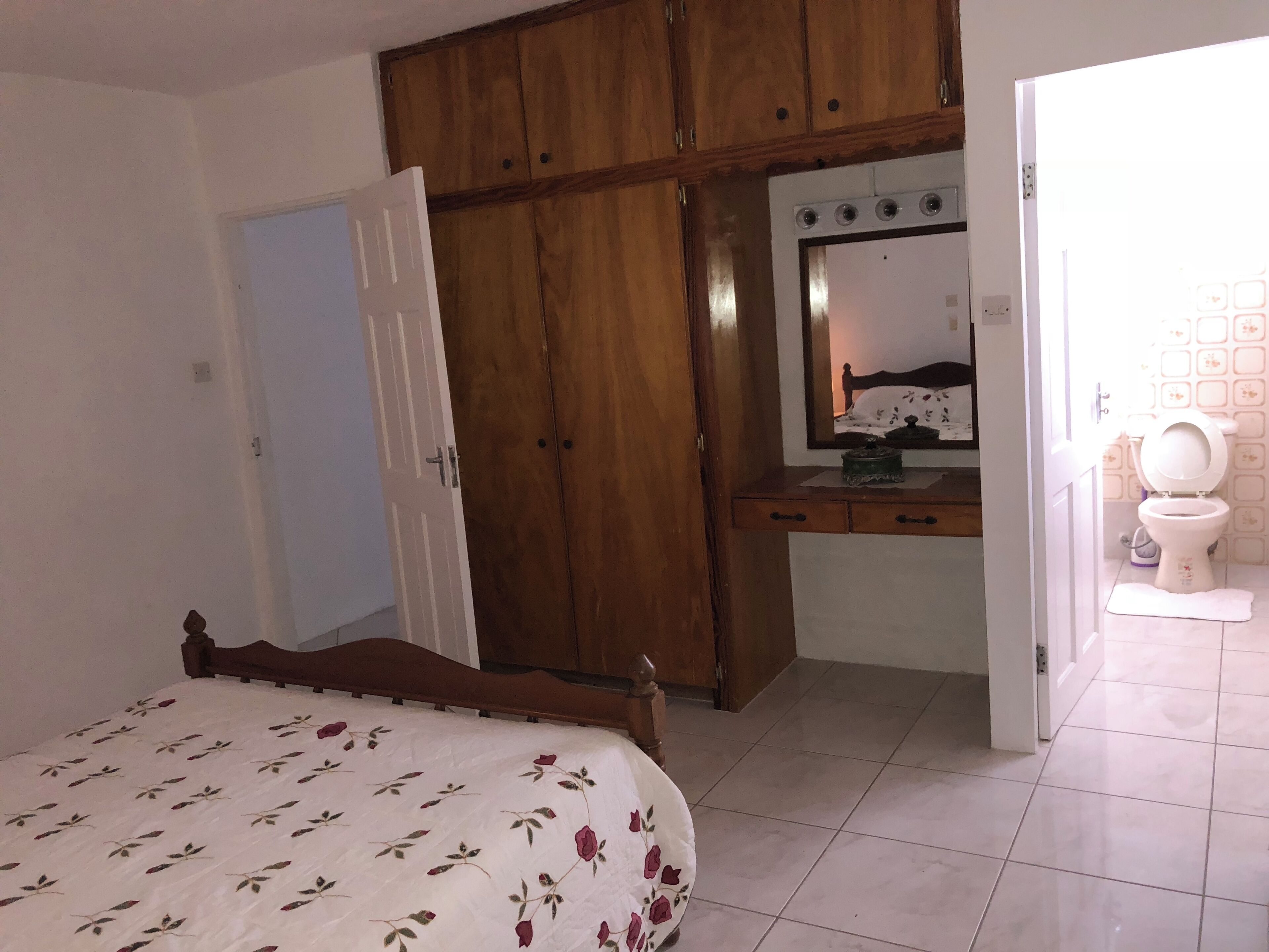 Un dormitorio con cama, armario de madera, escritorio con espejo y baño con inodoro.