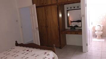 Un dormitorio con cama, armario de madera, escritorio con espejo y baño con inodoro.