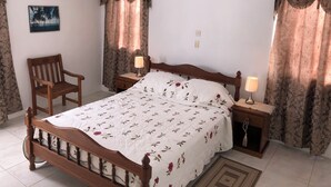 Ein Schlafzimmer mit einem hölzernen Bett, zwei Nachttischen mit Lampen, einem Sessel und Vorhängen.