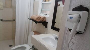 Un bany amb vàter, rentamig, dutxa i un assecador de cabells penjat a la paret.