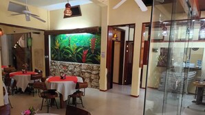 A restaurant with round tables, chairs, a mural, and a glass partition. - Hotel Museo Xibalba (Palenque)