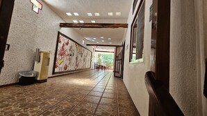 A hallway with patterned tiles, a wall-mounted trash bin, a door with a number, and a window. - Hotel Museo Xibalba (Palenque)