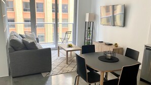 A modern living room with a grey sofa, a dining table with chairs, a small coffee table, a TV mounted on the wall, and a balcony with a view of buildings. - Modern studio in the heart of Downtown/Brickell Miami. Walk to Brickell. (Miami)