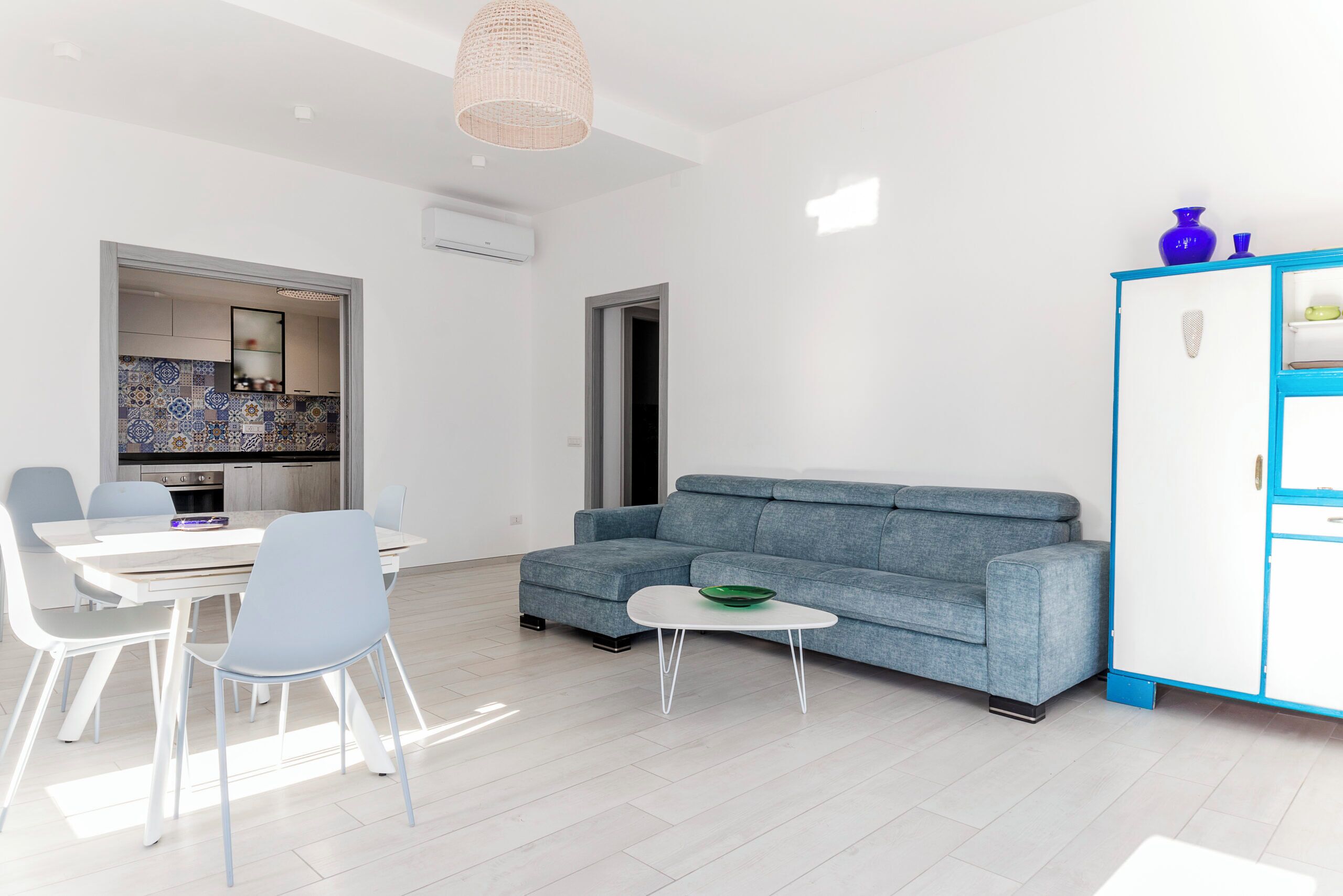 Un salon moderne comprenant un canapé, une table à manger, des chaises et une cuisine visible à travers une porte ouverte.
