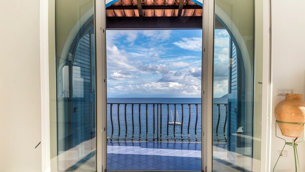Een open deur naar een balkon met uitzicht op zee en een zeilboot.