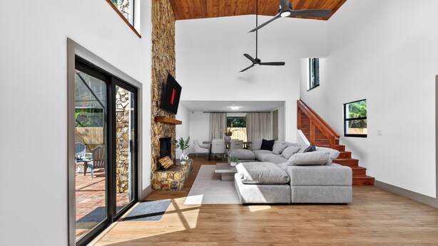 Ein großzügiger Wohnbereich mit Kamin, Sofa, Treppe und Blick ins Freie.