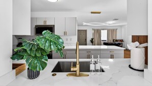 Eine moderne Küche mit weißen Schränken, einem goldenen Wasserhahn und einer großen, grünen Pflanze.