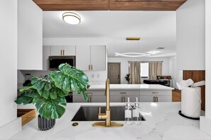 Eine moderne Küche mit weißen Schränken, einem goldenen Wasserhahn und einer großen, grünen Pflanze.