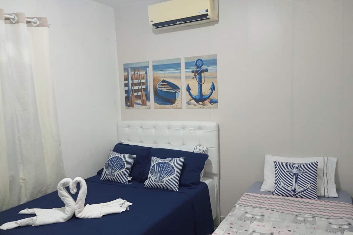 A bedroom with a bed, a nightstand, a wall-mounted air conditioner, and nautical-themed wall art.