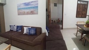 Una sala de estar con un sofá marrón, un cuadro de una playa y una zona de comedor con una mesa y sillas.
