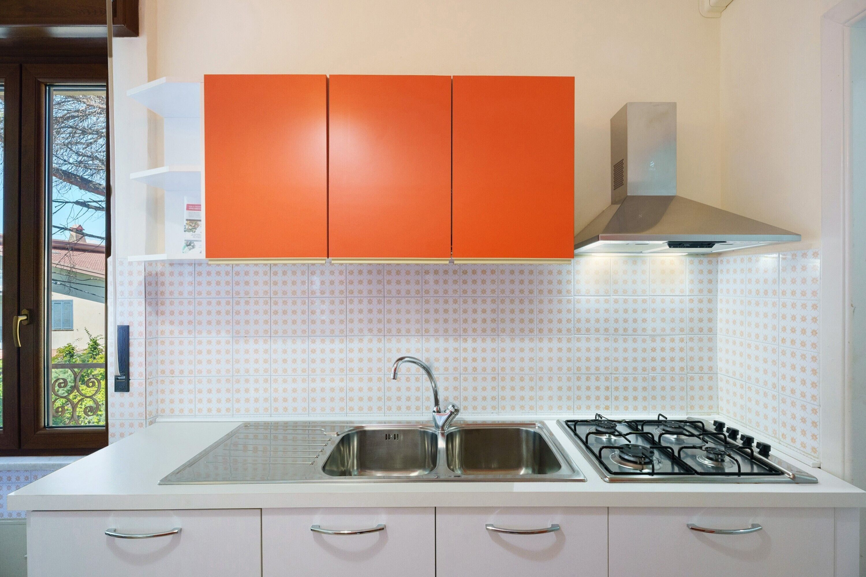 Une cuisine équipée d’un évier à deux bacs, d’une cuisinière à gaz et de meubles de rangement orange.