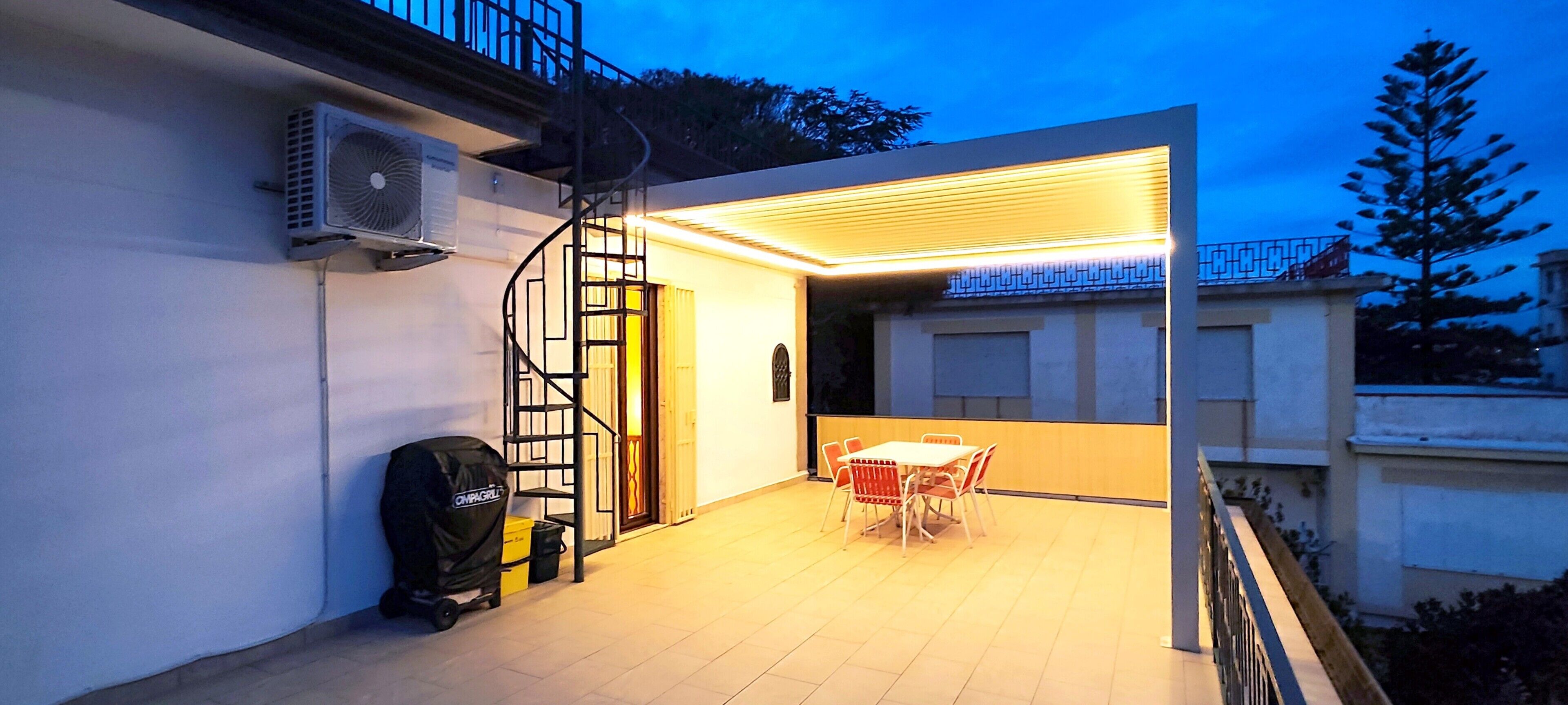 Un patio al aire libre con una mesa y sillas, una escalera en espiral y una unidad de aire acondicionado en la pared.