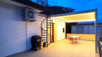 Un patio al aire libre con una mesa y sillas, una escalera en espiral y una unidad de aire acondicionado en la pared.