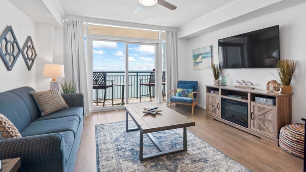 Ein Wohnzimmer mit einer Couch, einem Couchtisch, einem Fernseher und einem Balkon mit Gartenmöbeln.