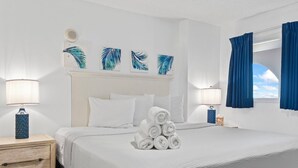 Ein ordentlich bezogenes Bett mit aufgerollten Handtüchern, einem weißen Kopfteil und Wandbildern.