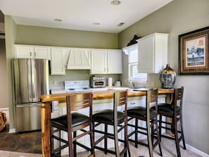 A kitchen with white cabinets, a stainless steel refrigerator, a stove, a toaster, and a vase on the counter.