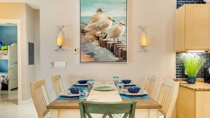 Een eetgedeelte met een tafel voor vier personen, twee wandlampen en een schilderij van meeuwen aan de muur.