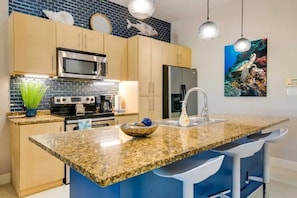 A modern kitchen with granite countertops, stainless steel appliances, and a large island with bar stools. - Beachside Condo w/ Pools, Hot Tubs & Balcony (South Padre Island)