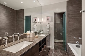 Un baño moderno con un amplio tocador, dos lavamanos, una ducha y cabina de ducha con paredes de vidrio.
