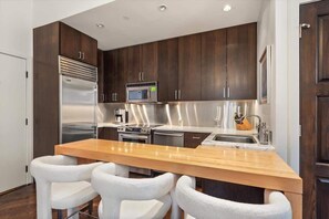 Una cocina moderna con armarios de madera oscura, electrodomésticos de acero inoxidable, una isla de madera con taburetes y un microondas integrado.