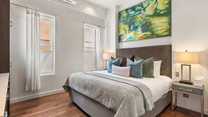 Une chambre moderne avec un grand lit, une tête de lit, une table de chevet et un climatiseur fixé au mur.