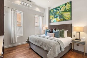 Un dormitorio moderno con una cama grande, cabecera, mesita de noche y aire acondicionado instalado en la pared.