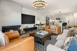 A modern living room with a fireplace, leather sofas, a coffee table, and a kitchen in the background. - Renovated 2 BR - 2 BA In Town with AC! (Aspen)