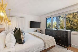A bedroom with a bed, a dresser, a TV, and a window with a view of trees. - Renovated 2 BR - 2 BA In Town with AC! (Aspen)