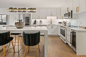 A modern kitchen with white cabinetry, a central island, black chairs, and gold accents. - Renovated 2 BR - 2 BA In Town with AC! (Aspen)