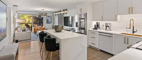 A modern kitchen with white cabinetry, a central island, and a dining area with black chairs.