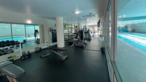Ett gym med löpband, styrketräningsmaskiner och en pool som syns genom glasväggen.