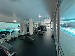 A gym with treadmills, weight machines, and a pool visible through the glass. - Stylish Downtown Condo with Free Parking + AC (Vancouver)