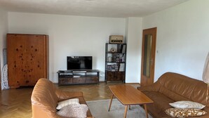Uma sala de estar com sofá, mesa de centro, televisão, estante e armário.