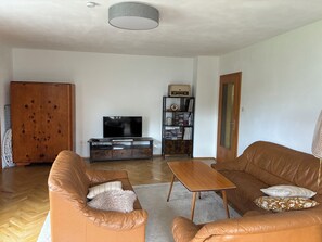 A living room with a sofa, a coffee table, a television, a bookshelf, and a wardrobe.