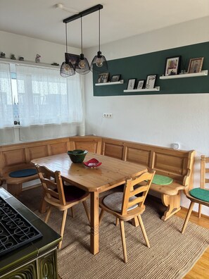 A dining area with a wooden table, chairs, and a kitchen area with a stove. - Cozy apartment with large garden and perfect location between the mountains and the sea (Liebenfels)