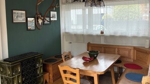 Uma sala de jantar com mesa de madeira, cadeiras, um lustre e um crânio de veado fixado na parede.